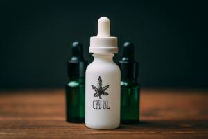 White glass bottle and two green bottles with text CBD Oil and Cannabis or hemp leaf sign, close up